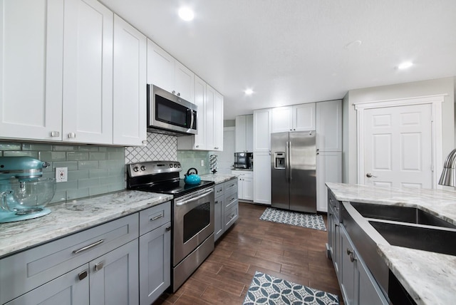 kitchen with sink, appliances with stainless steel finishes, white cabinetry, light stone counters, and tasteful backsplash