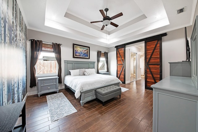 bedroom featuring a barn door, dark hardwood / wood-style floors, and a tray ceiling