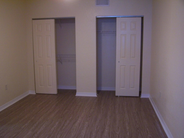 unfurnished bedroom with two closets and hardwood / wood-style flooring