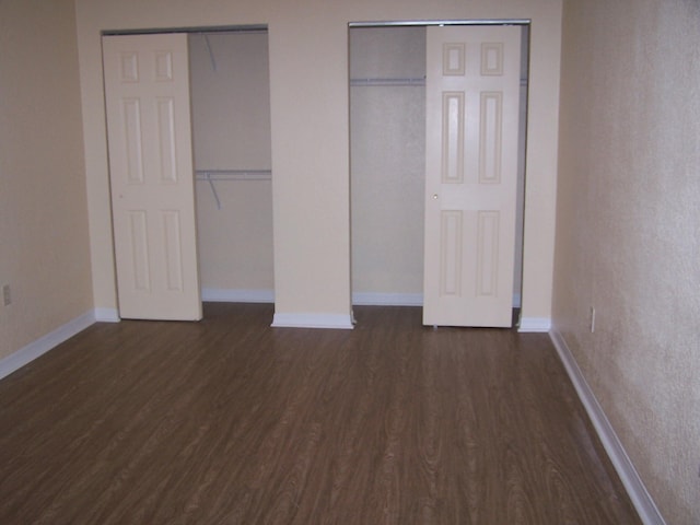 unfurnished bedroom with two closets and dark hardwood / wood-style floors