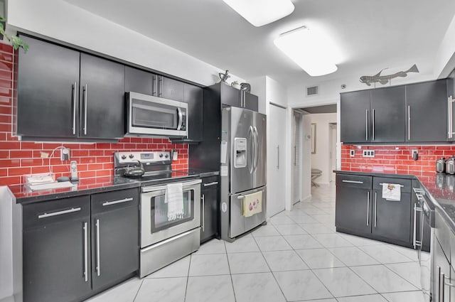 kitchen featuring stainless steel appliances, dark stone counters, light tile patterned floors, and decorative backsplash