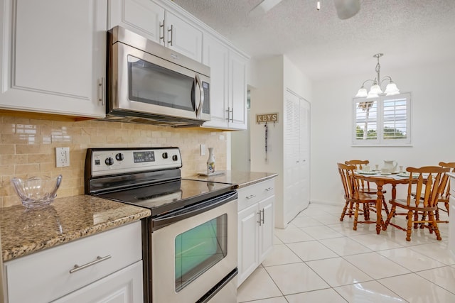 kitchen featuring light stone countertops, appliances with stainless steel finishes, white cabinetry, a chandelier, and light tile patterned flooring