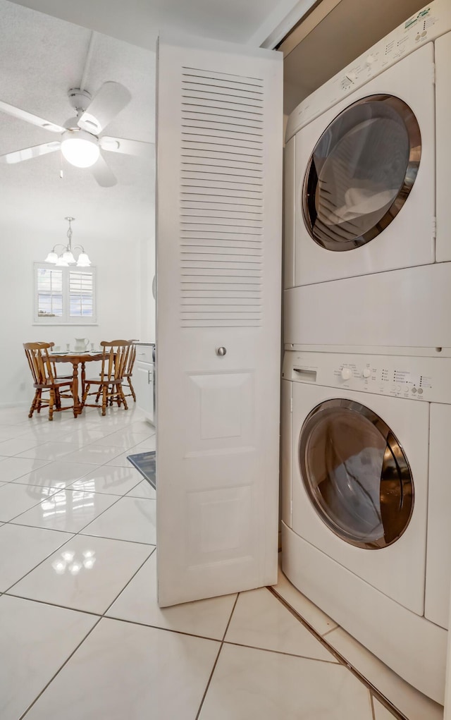 laundry room with tile patterned flooring, stacked washer and clothes dryer, and ceiling fan with notable chandelier