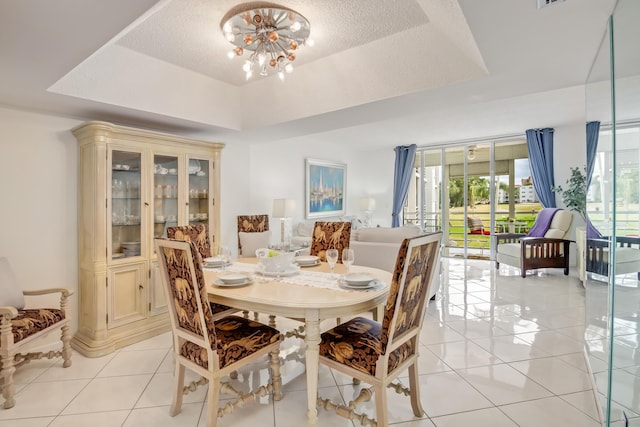 dining space with a textured ceiling, light tile patterned flooring, a raised ceiling, and a notable chandelier