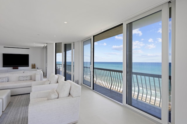 living room featuring floor to ceiling windows, a water view, and a beach view