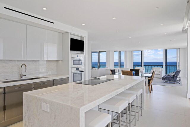 kitchen featuring light stone countertops, white cabinets, a wall of windows, backsplash, and black electric cooktop