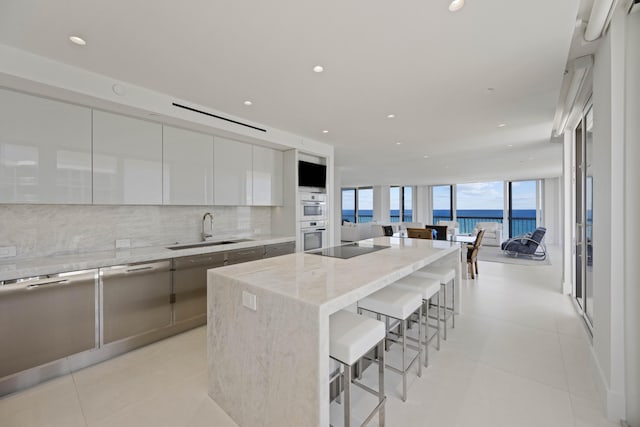 kitchen with light stone countertops, white cabinets, a kitchen island, a kitchen bar, and sink