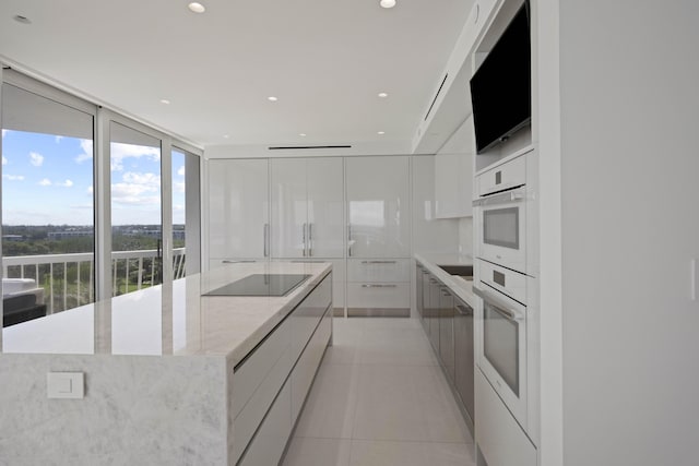 kitchen featuring white oven, white cabinets, a large island, light tile patterned flooring, and expansive windows