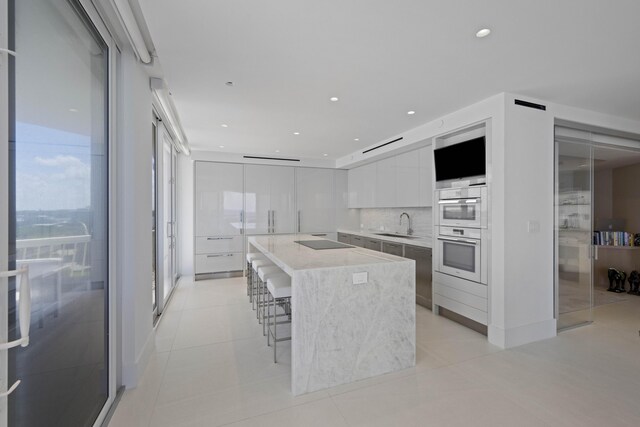 kitchen with a spacious island, white cabinets, black electric stovetop, sink, and a breakfast bar