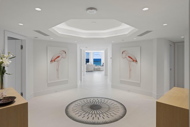 corridor with light tile patterned flooring and a tray ceiling