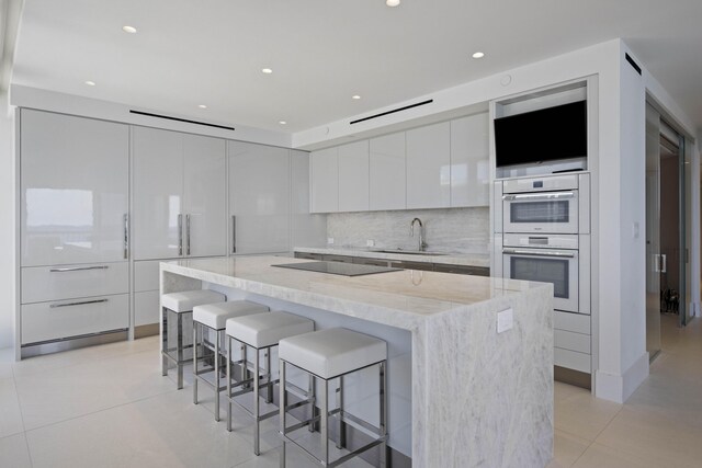 kitchen featuring white cabinetry, double wall oven, a breakfast bar area, sink, and a center island