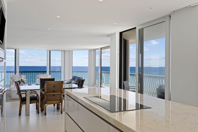 kitchen with a water view, white cabinets, expansive windows, and black electric cooktop