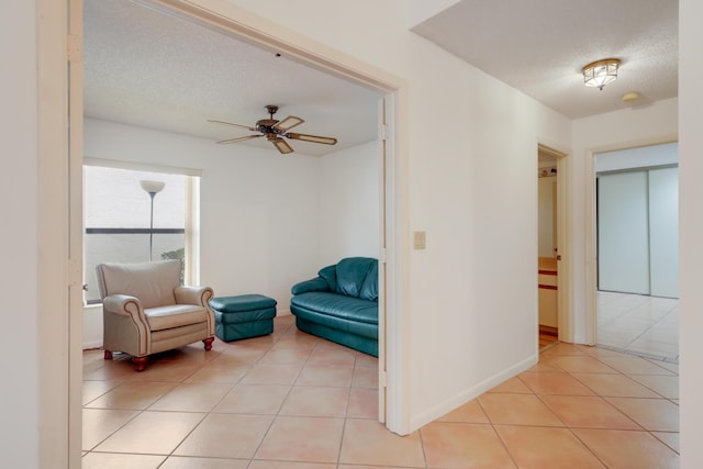 living area with a ceiling fan, a textured ceiling, baseboards, and light tile patterned floors