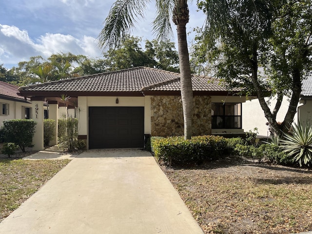 view of front of house featuring driveway, stucco siding, a garage, stone siding, and a tiled roof