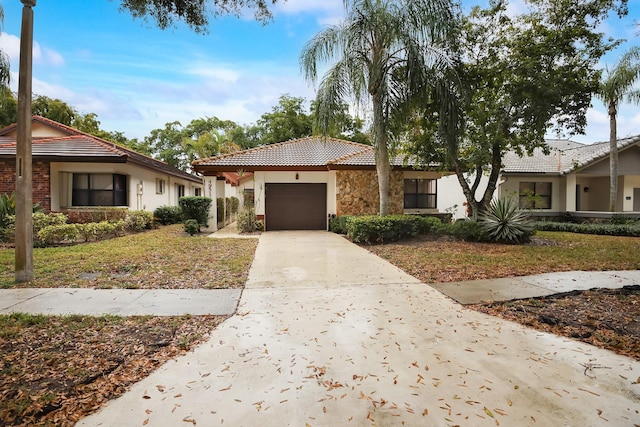 mediterranean / spanish home featuring stucco siding, concrete driveway, an attached garage, stone siding, and a tiled roof