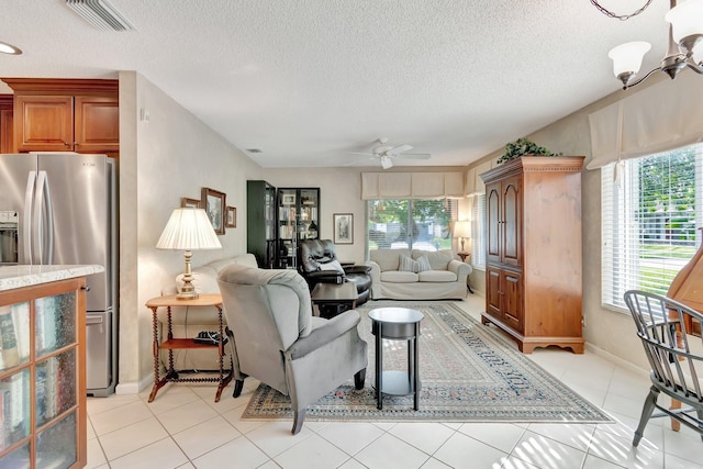 tiled living room with a textured ceiling, ceiling fan with notable chandelier, and plenty of natural light