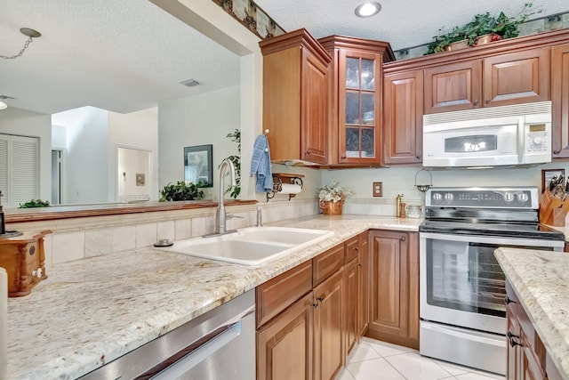 kitchen featuring light stone countertops, a textured ceiling, stainless steel appliances, sink, and light tile patterned floors