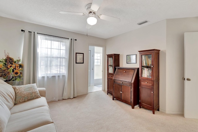 living area with ceiling fan, a textured ceiling, and light carpet