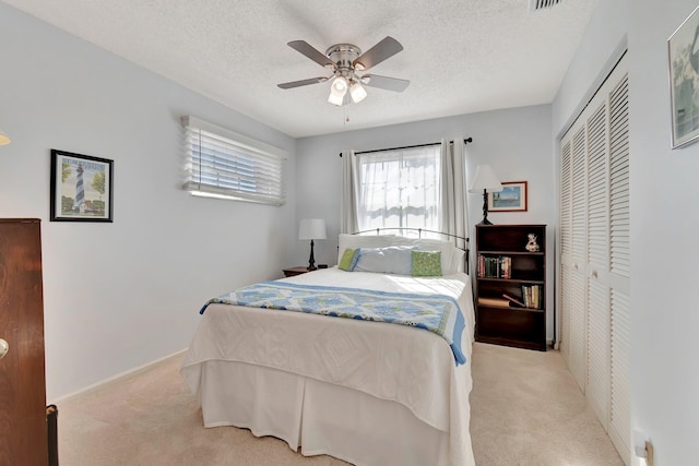 bedroom with a textured ceiling, ceiling fan, a closet, and light colored carpet