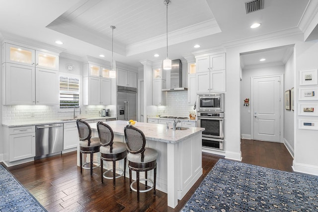 kitchen with built in appliances, wall chimney exhaust hood, a tray ceiling, and visible vents