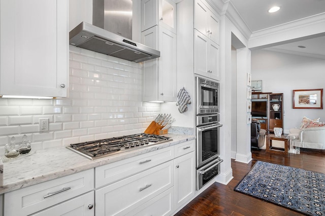 kitchen featuring dark wood-type flooring, wall chimney range hood, appliances with stainless steel finishes, a warming drawer, and tasteful backsplash