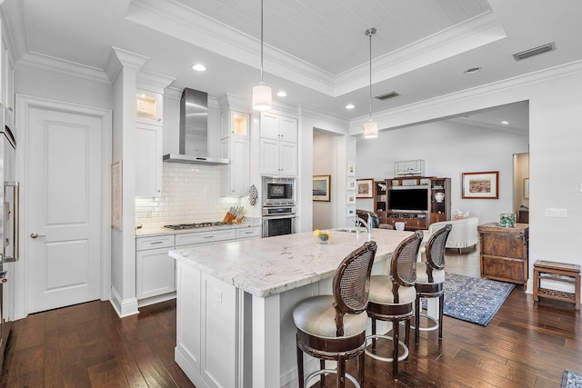 kitchen with visible vents, white cabinets, wall chimney range hood, appliances with stainless steel finishes, and a raised ceiling