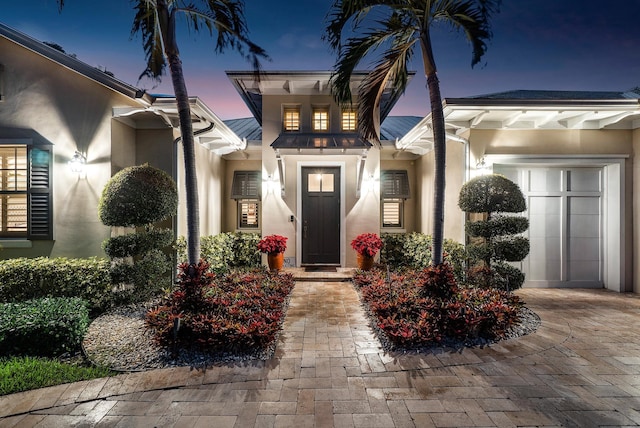 view of exterior entry with decorative driveway, an attached garage, and stucco siding