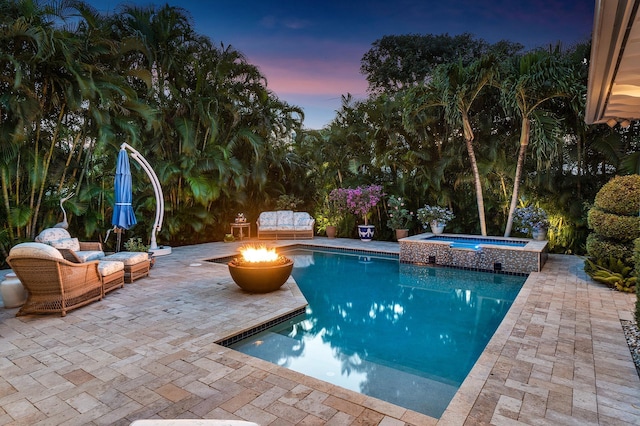 pool at dusk with an outdoor fire pit, a pool with connected hot tub, and a patio