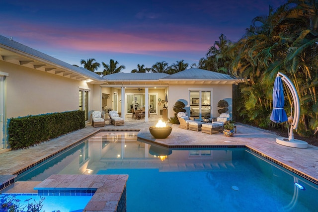 back of property at dusk with a fire pit, an outdoor pool, a ceiling fan, a patio area, and stucco siding