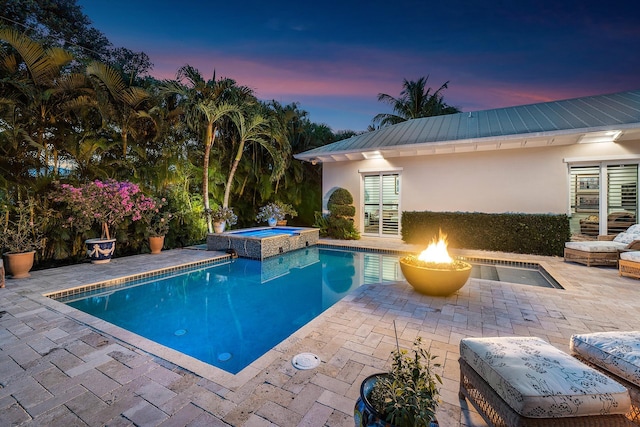 pool at dusk featuring a pool with connected hot tub and a patio