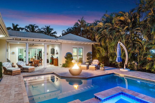 pool at dusk with an in ground hot tub, a fire pit, an outdoor pool, and a patio