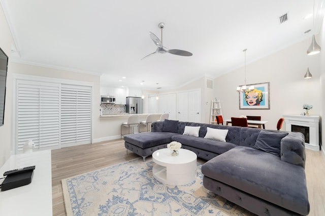 living room with crown molding, ceiling fan with notable chandelier, vaulted ceiling, and light hardwood / wood-style flooring