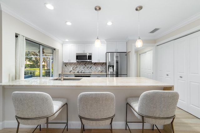 kitchen featuring decorative light fixtures, sink, stainless steel appliances, and white cabinetry