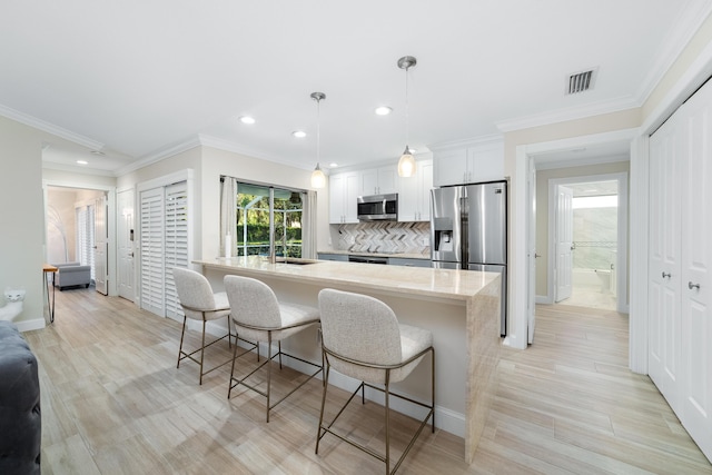 kitchen with decorative light fixtures, white cabinetry, stainless steel appliances, light stone counters, and a breakfast bar