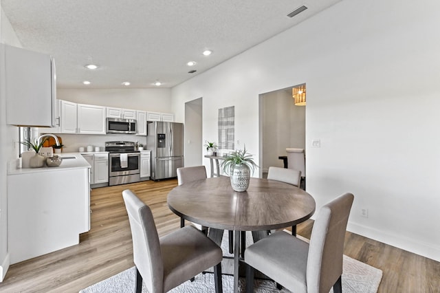 dining room with vaulted ceiling, light hardwood / wood-style floors, sink, and a textured ceiling