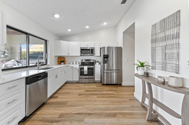 kitchen featuring lofted ceiling, sink, appliances with stainless steel finishes, white cabinets, and light wood-type flooring