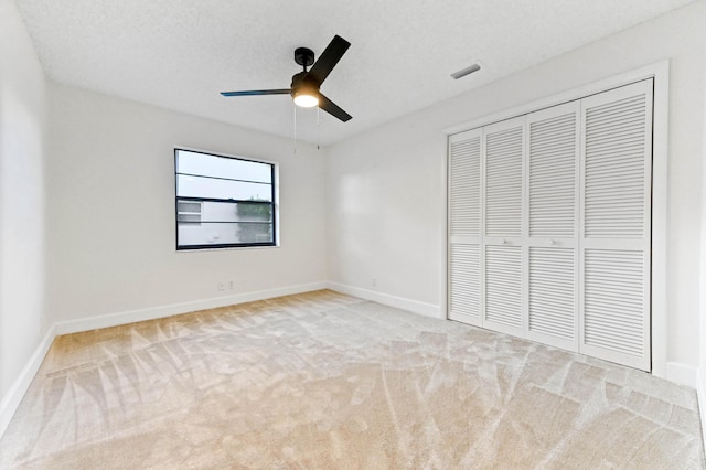 unfurnished bedroom with ceiling fan, light colored carpet, a closet, and a textured ceiling