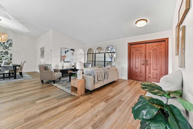 living room with an inviting chandelier, lofted ceiling, a textured ceiling, and light wood-type flooring