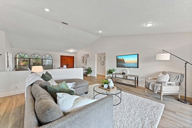 living room featuring vaulted ceiling, a textured ceiling, and light hardwood / wood-style floors