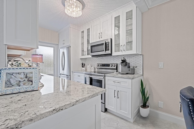 kitchen featuring white cabinets, appliances with stainless steel finishes, tasteful backsplash, an inviting chandelier, and light stone counters