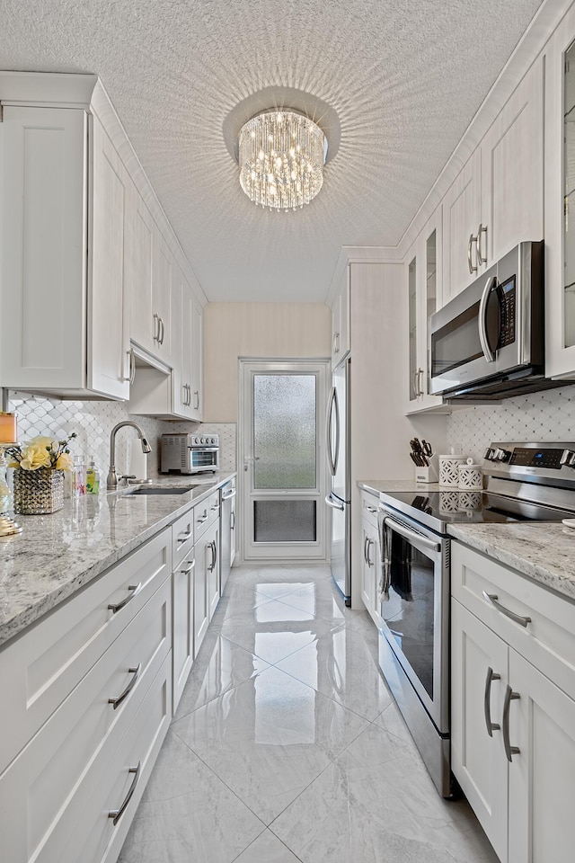 kitchen featuring an inviting chandelier, white cabinetry, stainless steel appliances, light stone counters, and sink