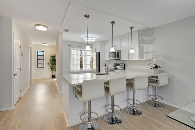 kitchen with kitchen peninsula, stainless steel appliances, decorative light fixtures, white cabinets, and a breakfast bar