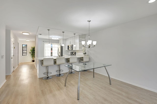 kitchen featuring light hardwood / wood-style floors, kitchen peninsula, appliances with stainless steel finishes, decorative light fixtures, and a breakfast bar