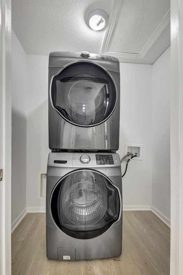 washroom with stacked washing maching and dryer, crown molding, a textured ceiling, and light hardwood / wood-style flooring