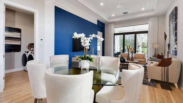 dining room featuring ceiling fan, washing machine and dryer, a tray ceiling, and hardwood / wood-style flooring