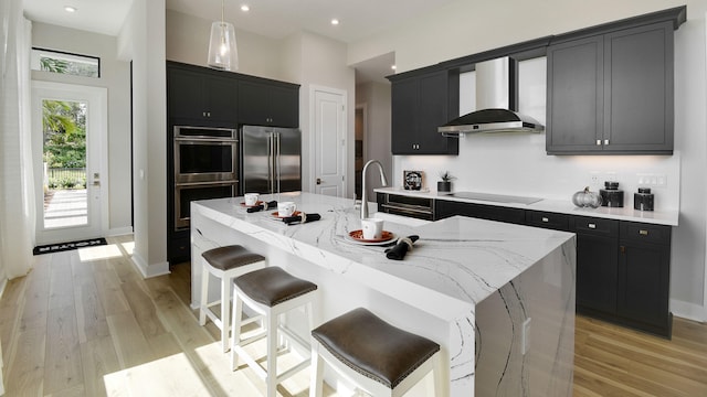 kitchen with pendant lighting, sink, an island with sink, stainless steel appliances, and wall chimney exhaust hood