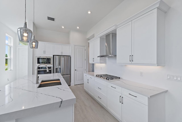 359 SE Via Sangro, Port Saint Lucie, FL 34952 - kitchen with stainless steel appliances, wall chimney range hood, a sink, white cabinetry, and light wood finished floors