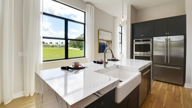 kitchen featuring decorative light fixtures, sink, appliances with stainless steel finishes, and an island with sink