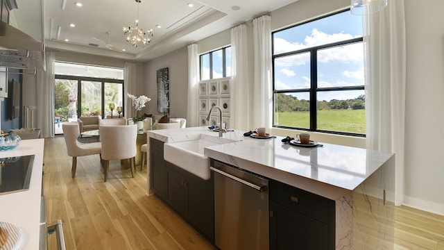 kitchen featuring a center island with sink, a tray ceiling, dishwasher, hanging light fixtures, and sink