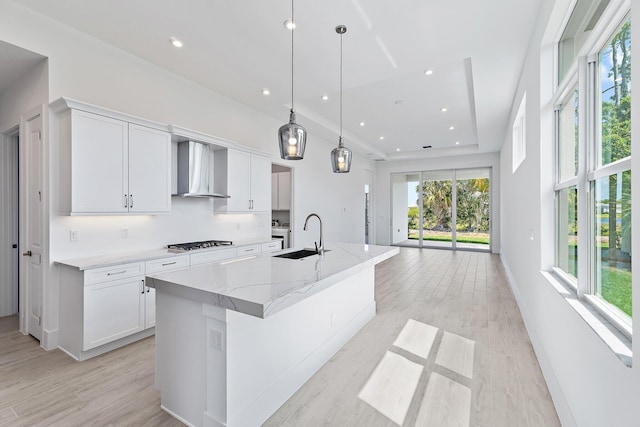 359 SE Via Sangro, Port Saint Lucie, FL 34952 - kitchen featuring wall chimney exhaust hood, gas stovetop, a sink, white cabinets, and a kitchen island with sink